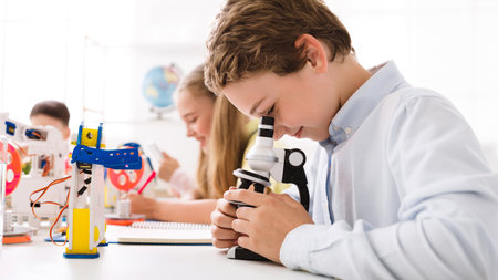 Young Boy Looking Through a Microscope in a Classroom Settingの写真素材