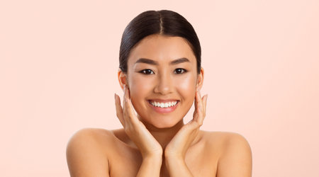 Young Woman With Long Black Hair Smiling, Touching Her Faceの写真素材