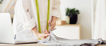 Focused tailor cutting fabric with scissors, sewing costume