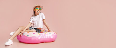 Young Woman Wearing Sunglasses And Hat Sitting On Pink Donutの写真素材