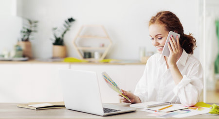 Woman Talking on Phone and Reviewing Documents at Deskの写真素材