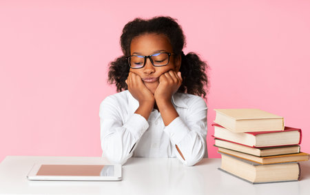 Afro Schoolgirl Sitting Between Tablet And Books On Yellow Backgroundの写真素材