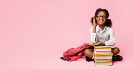 African Schoolgirl Raising Hand Sitting At Books Over Yellow Backgroundの写真素材