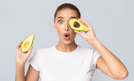 Positive Woman Holding Avocado Covering Eye Having Fun, Studio Shotの写真素材