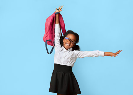 Joyful African Schoolgirl Posing With Backpack Over Yellow Studio Backgroundの写真素材