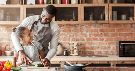 Cheerful black father teaching daughter cutting veggiesの写真素材