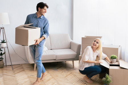 Man Carrying Box While Woman Unpacks In New Apartment