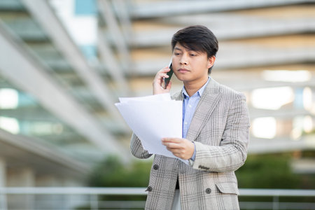 Businessman on Phone Reviewing Documents in Urban Settingの写真素材