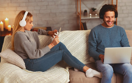 Positive Spouses Using Laptop And Tablet Wearing Earphones At Homeの写真素材