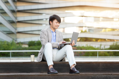Young Man Working on Laptop Outside Modern Buildingの写真素材
