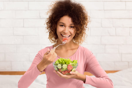 Pregnancy, healthy food concept. Afro woman eating vegetable saladの写真素材