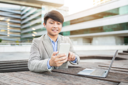 Man Using Smartphone While Sitting at Outdoor Table With Laptopの写真素材
