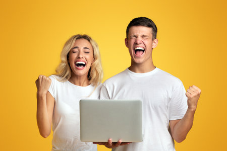 Excited young couple celebrating win with laptopの写真素材