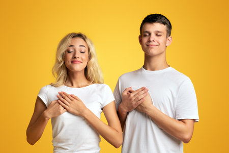 Grateful young couple keeping both palms on chest, expressing appreciationの写真素材