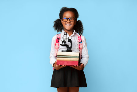Happy african girl holding books and microscope learning, yellow backgroundの写真素材