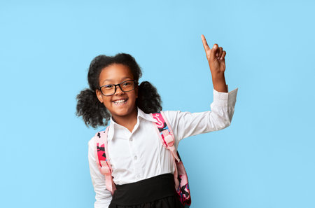 Smiling Schoolgirl Pointing Finger Up Having Question Over Yellow Backgroundの写真素材