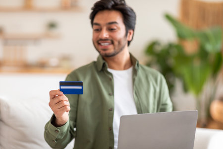Smiling Man Holding Credit Card While Using Laptop at Homeの写真素材