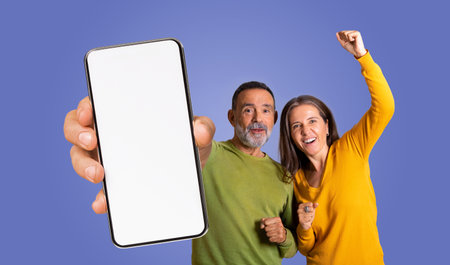 Excited Couple Holding Smartphone With Blank Screen Against Purple Background