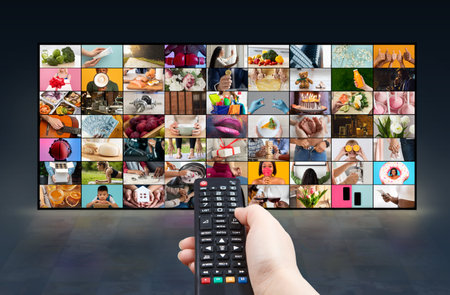 Hand Holding Remote Control Over Large Television Displaying Multiple Imagesの写真素材