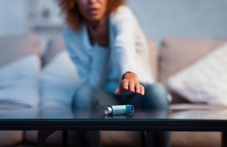 Girl suffering asthma attack reaching inhaler sitting on a couch in the living room at homeの写真素材