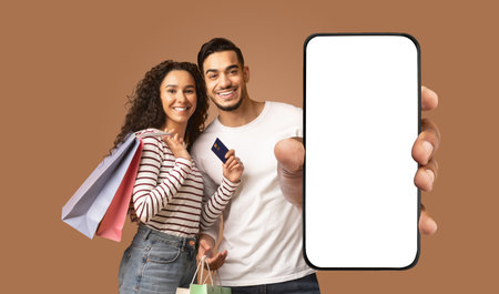 Happy Couple Holding Shopping Bags and Smartphone With White Screen