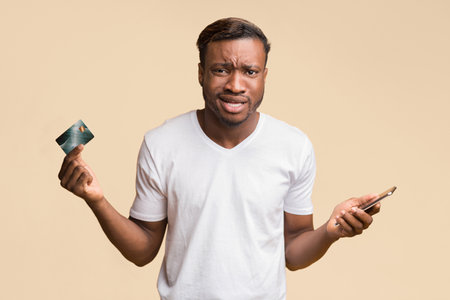 Confused Guy Holding Smartphone And Credit Card Posing In Studioの写真素材