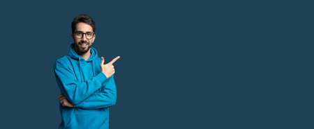 Young Man in Blue Hoodie Pointing Against a Solid Background