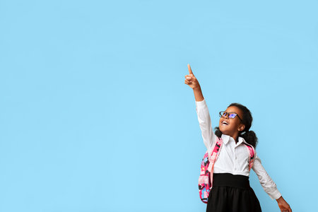 Afro Schoolgirl Pointing Finger Showing Something Over Yellow Backgroundの写真素材