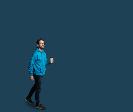 Man in Blue Hoodie Walks Confidently While Holding Coffee Cupの写真素材