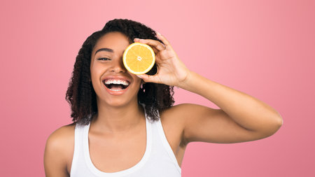 Happy black girl holding halves of orange near face