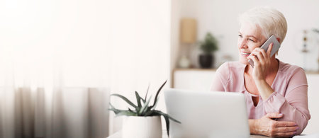 Positive old woman talking by phone with clientsの写真素材