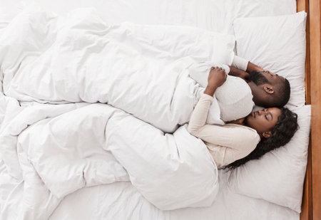 Afro couple hugging while sleeping together in bed, top view