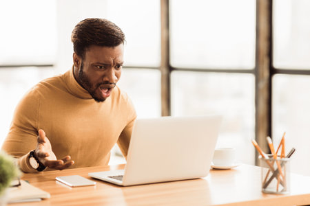 Shocked surprised balck guy using pc at workの写真素材