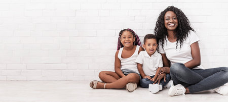 Black millennial mom sitting on floor with daughter and son