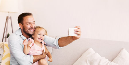 Smiling dad and little girl taking selfie at homeの写真素材
