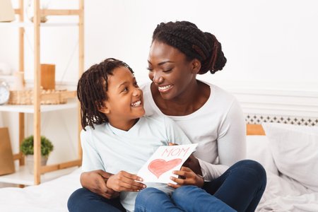 Afro kid congratulating her mom sitting on the bedの写真素材