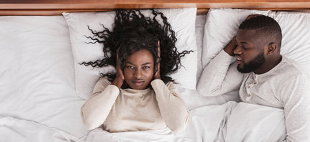 Black woman closing ears tired of her husbands noisy snoring.