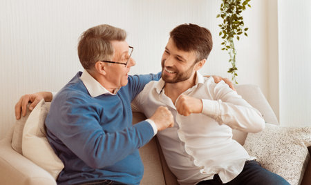 Son And Father Bumping Fists Sitting On Couch At Homeの写真素材