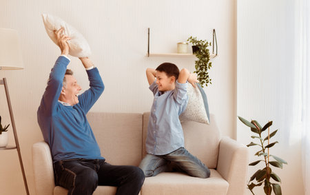 Happy Grandfather And Grandson Fighting With Pillows Sitting On Sofaの写真素材