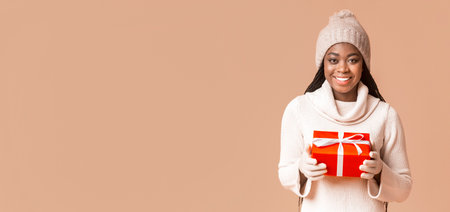 Beautiful black woman in winter hat and gloves holding gift