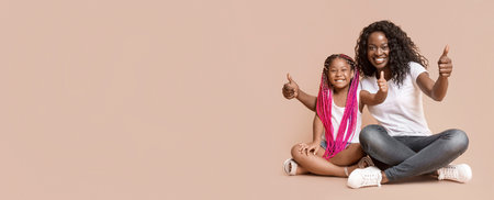Mother and Daughter Gesturing Thumbs Up Over Yellow Background.の写真素材