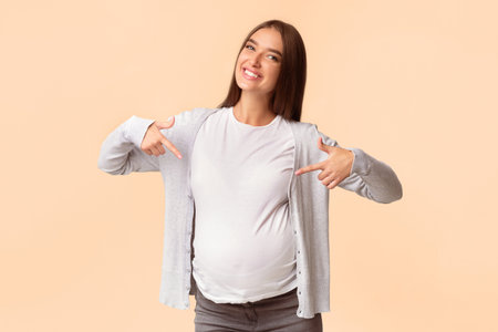 Smiling Pregnant Woman Pointing Fingers Showing Her Belly, Studio Shotの写真素材