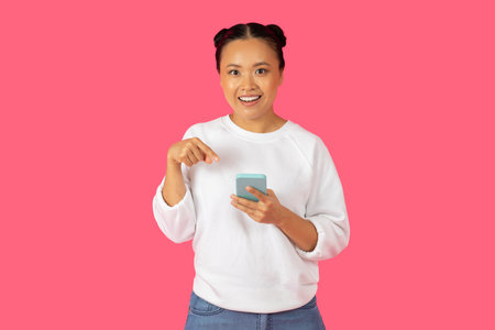 Smiling young woman using smartphone against a pink background indoors