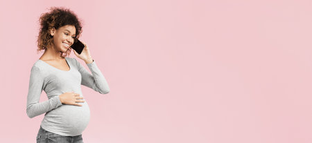 African-american expectant woman having phone conversation, pink backgroundの写真素材
