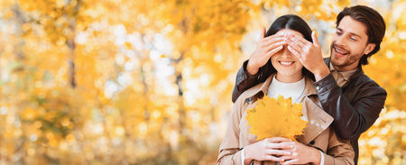 Man closing eyes of his girlfriend, dating in autumn parkの写真素材