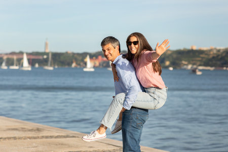 Happy couple enjoying playful moment by waterfront on sunny dayの写真素材