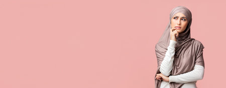 Pensive muslim girl thinking and looking away on pink studio backgroundの写真素材