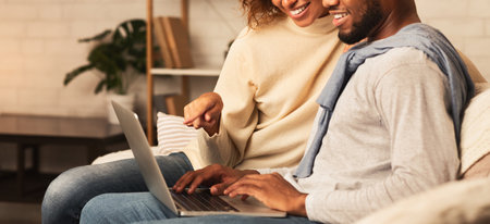 Happy afro spouses using laptop, spending weekend at homeの写真素材