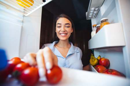 Young woman taking fresh healthy vegetables from fridgeの写真素材