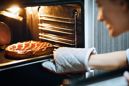Happy housewife taking fresh pie out of oven at home